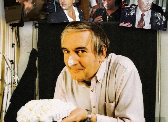 Noël Godin, facétieux belge au visage youpissant, tenant une tarte à la crème entre ses doigts.